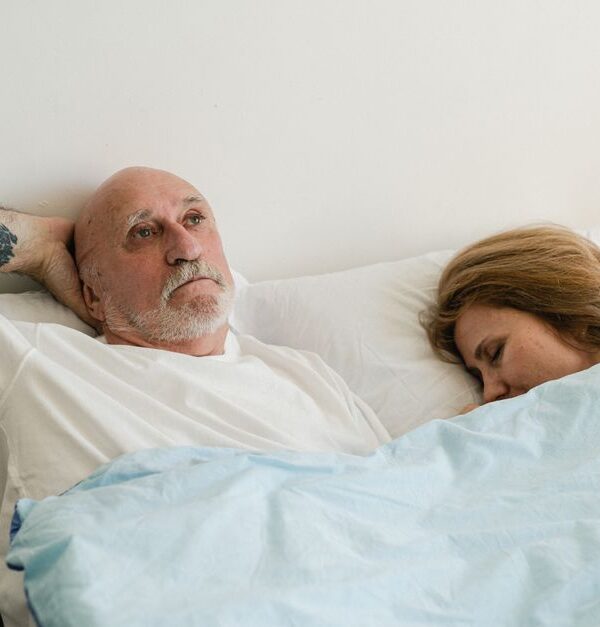 A man lies awake deep in thought beside his sleeping partner, keeping his private reflections to himself.