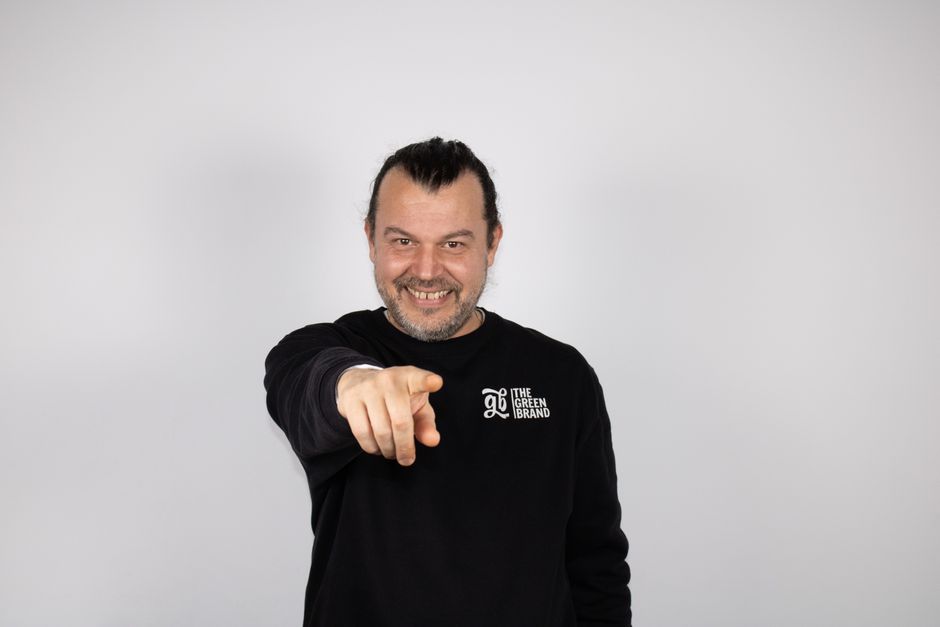 A man grinning slyly while pointing at the camera, as if caught in a white lie.