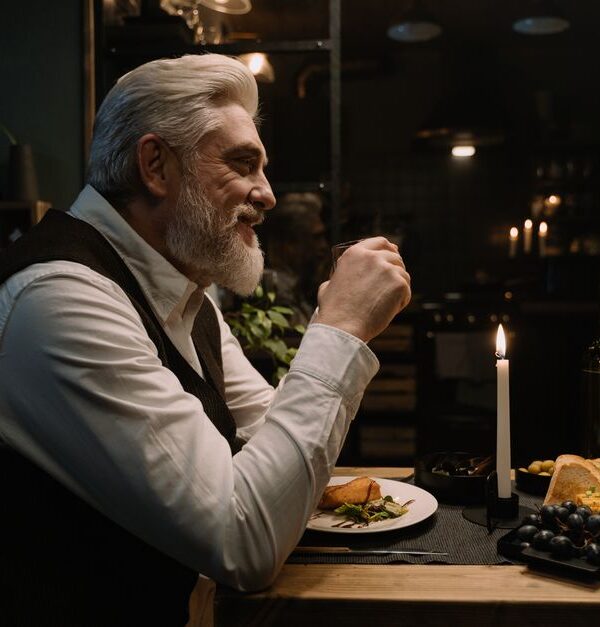 A man over 50 enjoys a romantic candlelit dinner, reflecting the thoughtfulness that keeps relationships lasting for decades.