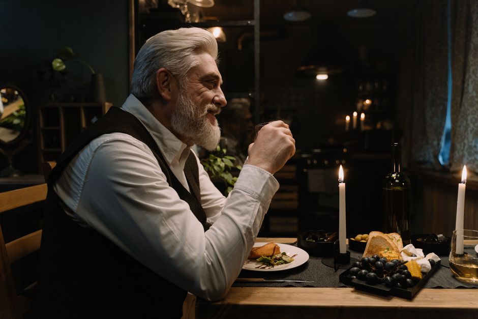 A man over 50 enjoys a romantic candlelit dinner, reflecting the thoughtfulness that keeps relationships lasting for decades.