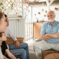 An older parent sits with crossed arms while his adult child's family gathers around, illustrating tension that can arise from saying the wrong things to adult children.