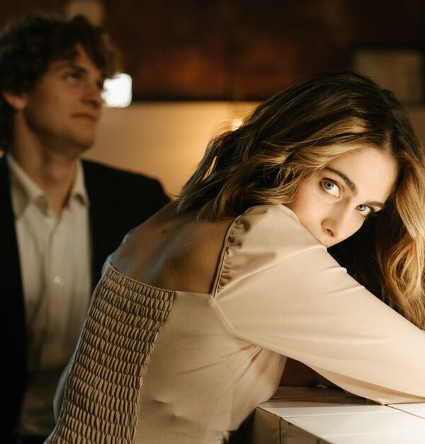 A woman at a bar glances back invitingly over her shoulder while a man nearby looks her way, hinting she wants him to approach.