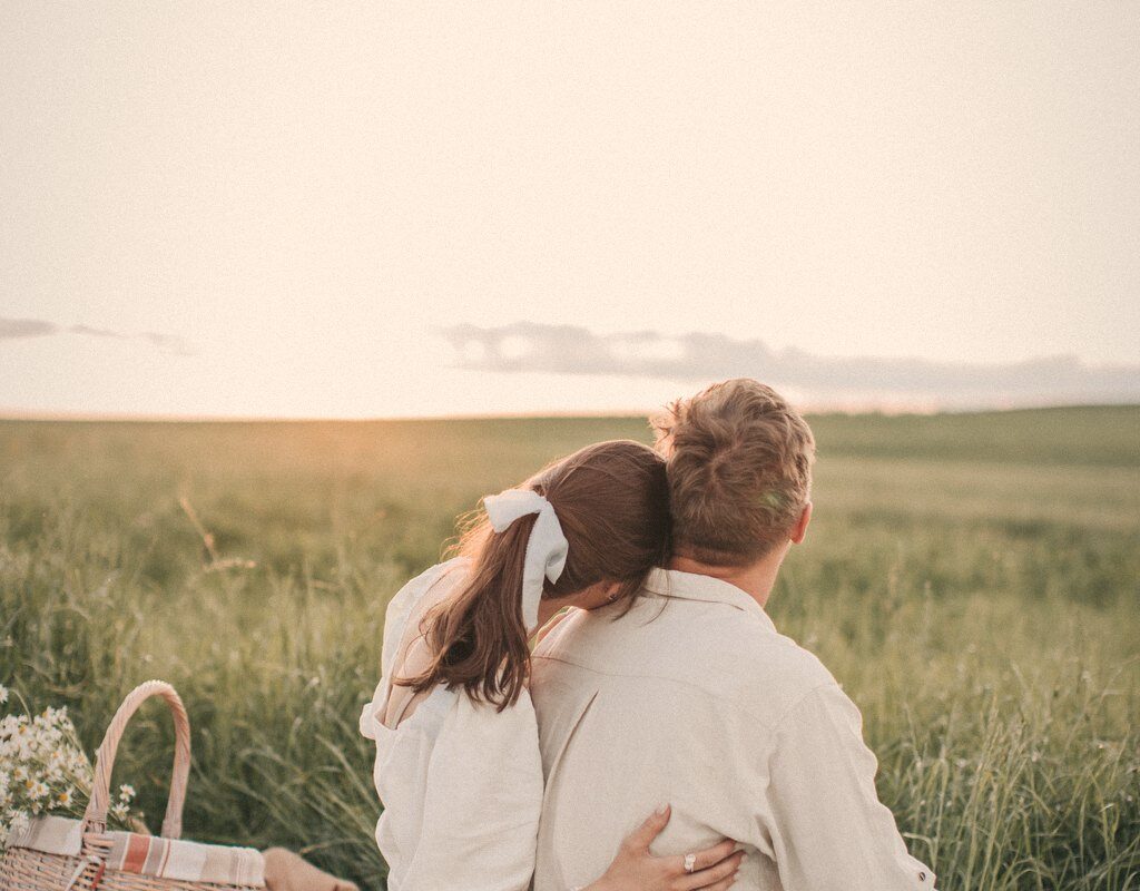 A couple sitting close on a picnic blanket at sunset