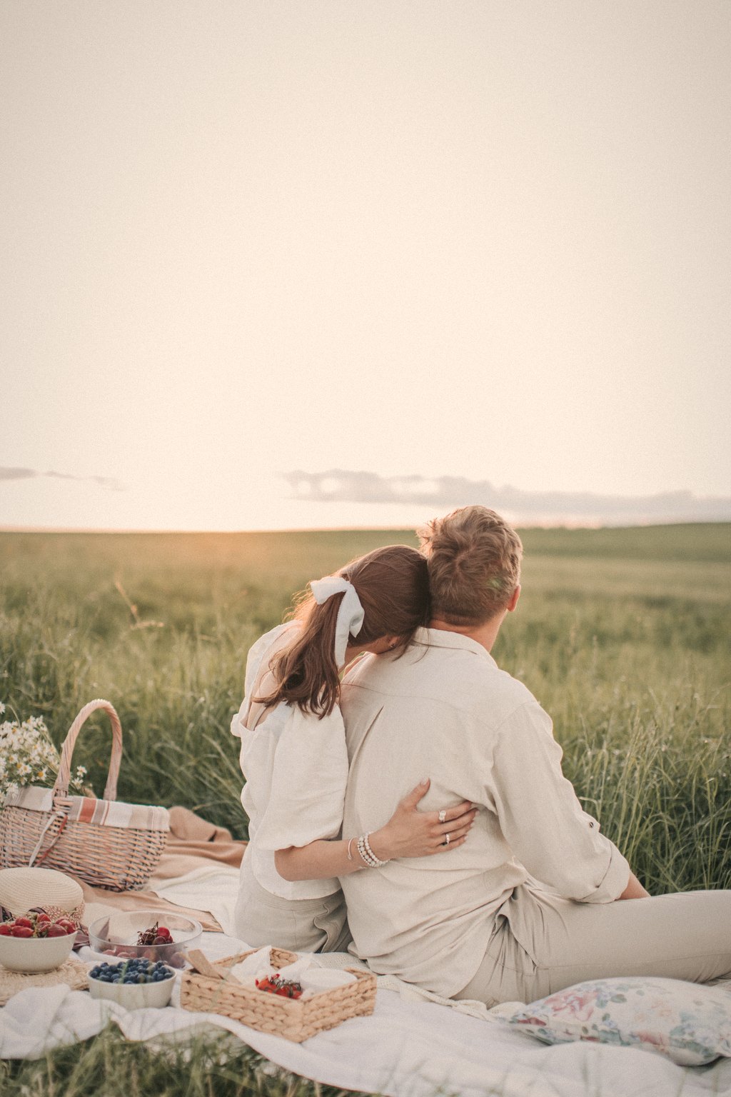 A couple sitting close on a picnic blanket at sunset