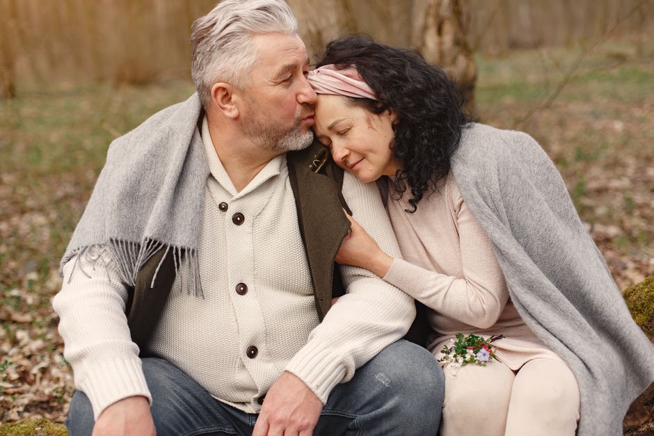 A mature husband gently kisses his wife's forehead, showing a tender, affectionate gesture of love.