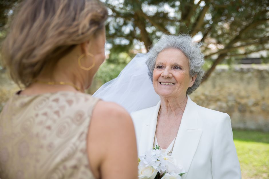 An older bride smiles affectionately at a loved one, sharing a heartfelt moment before her wedding.