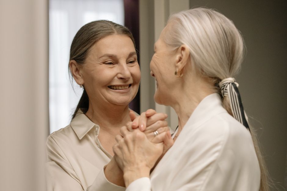 Two women over 50 smiling and holding hands, sharing a warm moment of connection and understanding.
