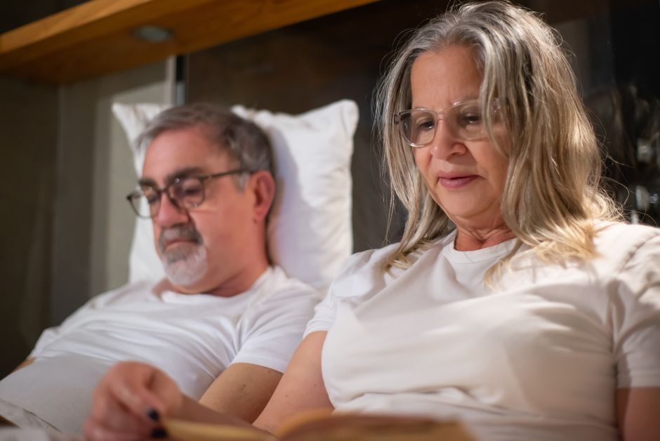 An older couple reads together in bed before settling in to sleep at the same time, just like couples from the '60s.