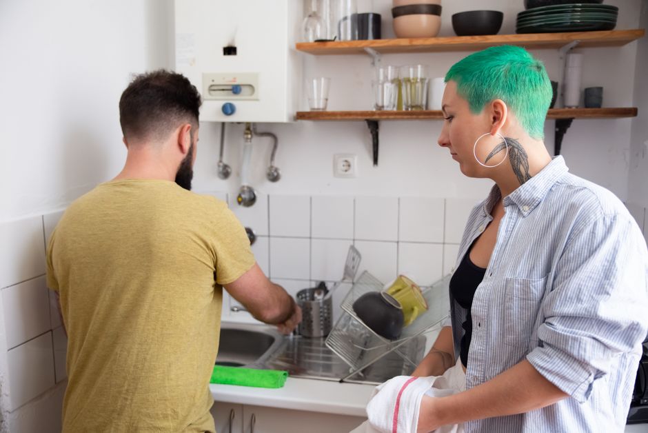 A couple washing dishes side by side at the kitchen sink, embracing an old-fashioned habit of doing chores together
