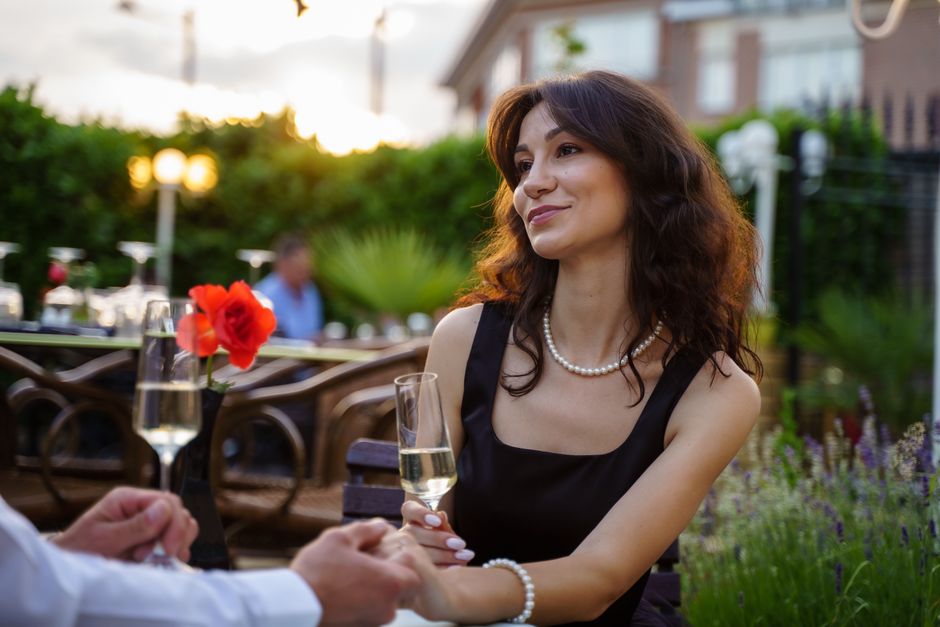 A couple dressed up for a romantic evening out, holding hands over champagne, embracing the old-fashioned habit of making an effort to look nice for each other