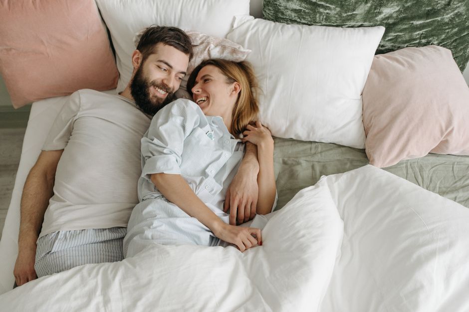 A happy couple smiling at each other in bed, embracing the old-fashioned habit of greeting each other warmly each morning