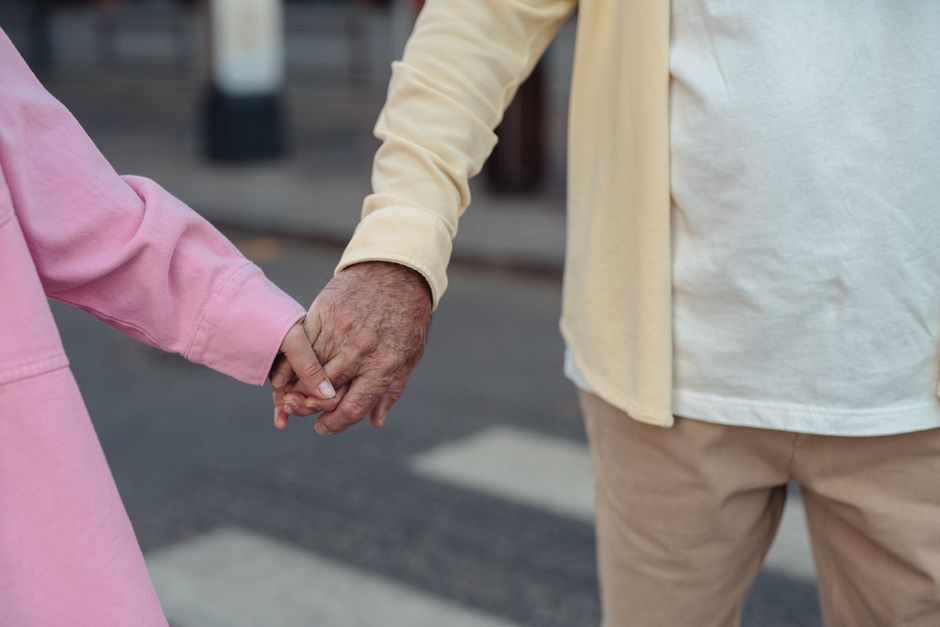 An older couple holds hands while walking together outside, a simple habit still cherished since the '60s