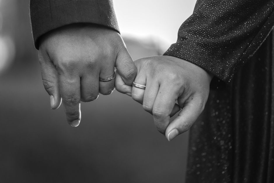 An older married couple link pinky fingers in a promise gesture, symbolizing the small vows that keep a marriage strong.