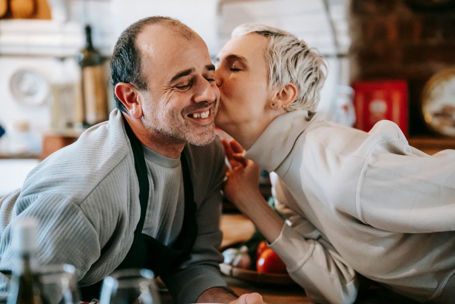 A couple sharing a sweet kiss in the kitchen, the kind of small affectionate gesture reminiscent of leaving a loving note for your spouse