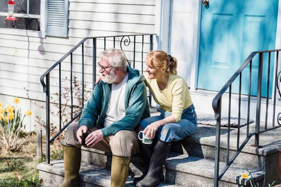An older couple relaxes together on their porch steps after a meal, sharing coffee and conversation outside.