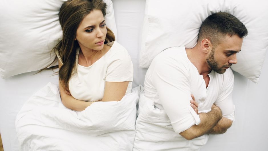 A couple lying in bed upset with each other, illustrating the importance of resolving arguments before falling asleep, a classic '60s marriage habit.