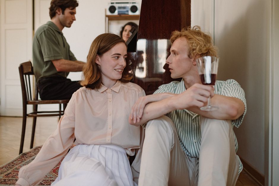 A couple interacts closely while other people are present nearby in the same room.