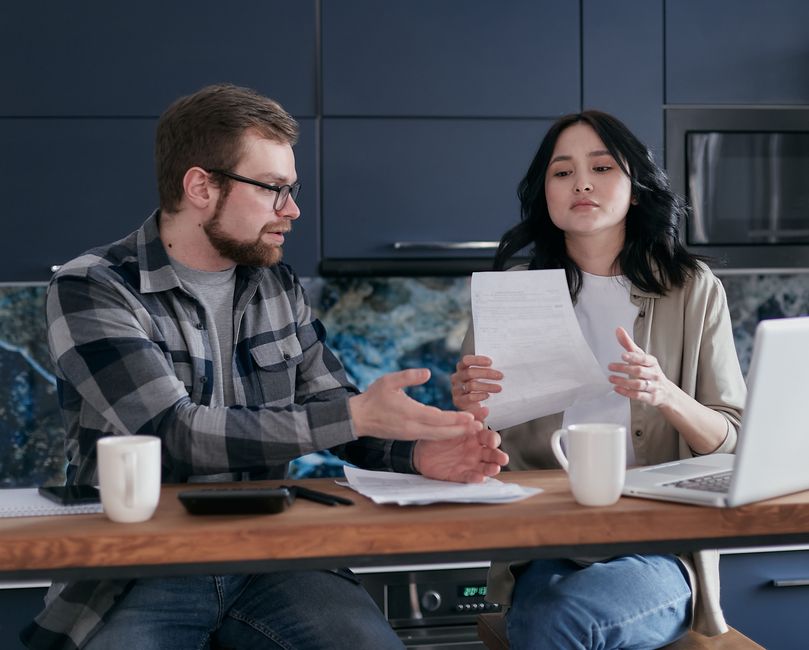 A couple sits at the kitchen table buried in bills and paperwork instead of connecting emotionally.