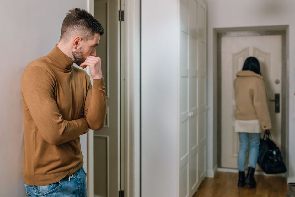 A woman heads out the door alone while her partner stands apart, lost in thought, reflecting how couples stop inviting each other along.