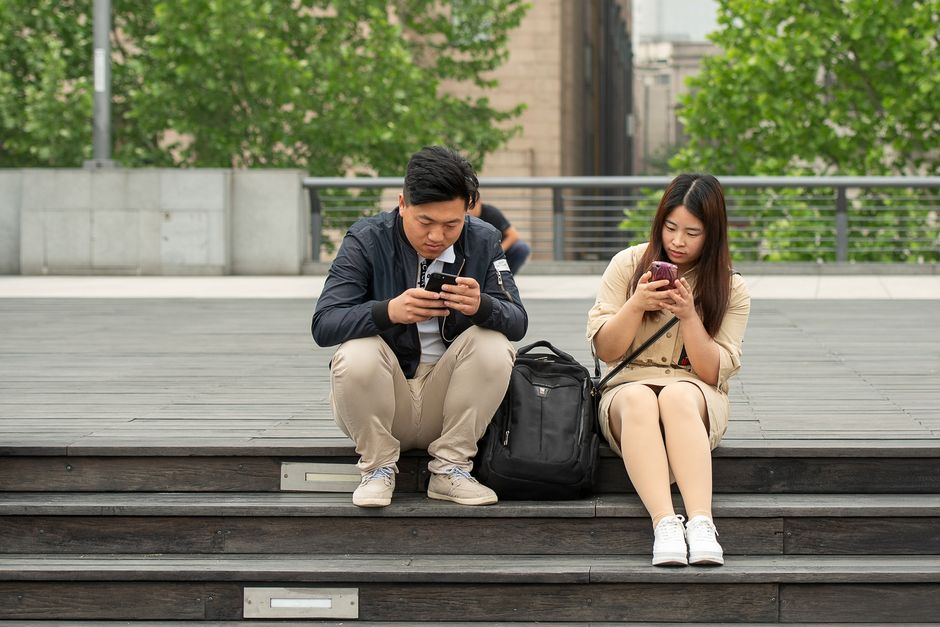 A couple sits apart on steps, each lost in their own phone instead of connecting with one another.