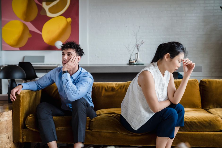 A couple sits silently apart on a couch, each avoiding eye contact, reflecting a relationship where the fighting has stopped and emotional distance has taken over.