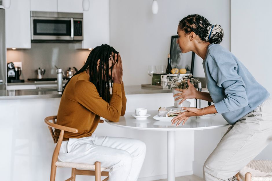 A tense couple argues at the kitchen table, their once-playful banter now turning sharp and cutting.