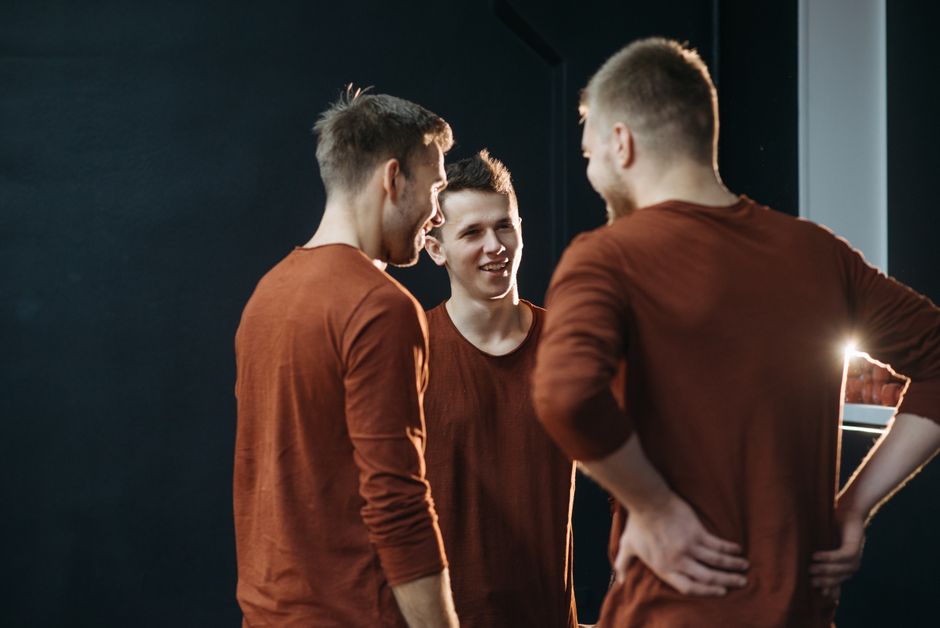 A group of guy friends huddled together whispering and glancing over, acting a bit odd as someone approaches.