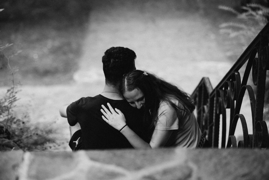A woman quietly comforts her partner with a gentle embrace, offering the emotional support he may not ask for but is willing to accept.