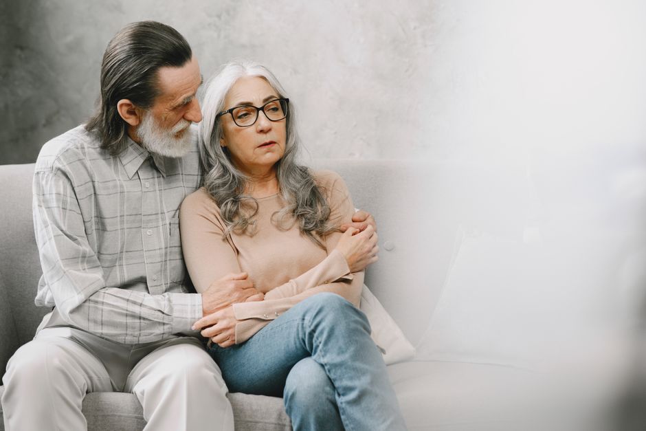 An older man gently comforts his worried wife, reflecting the quiet fear of becoming a burden to a loved one.
