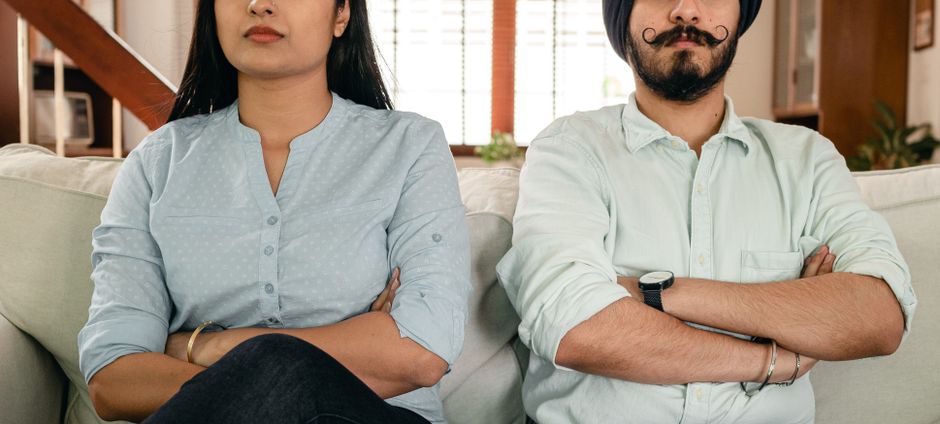 A husband and wife sit side by side with arms crossed, emotionally distant and silent instead of arguing.
