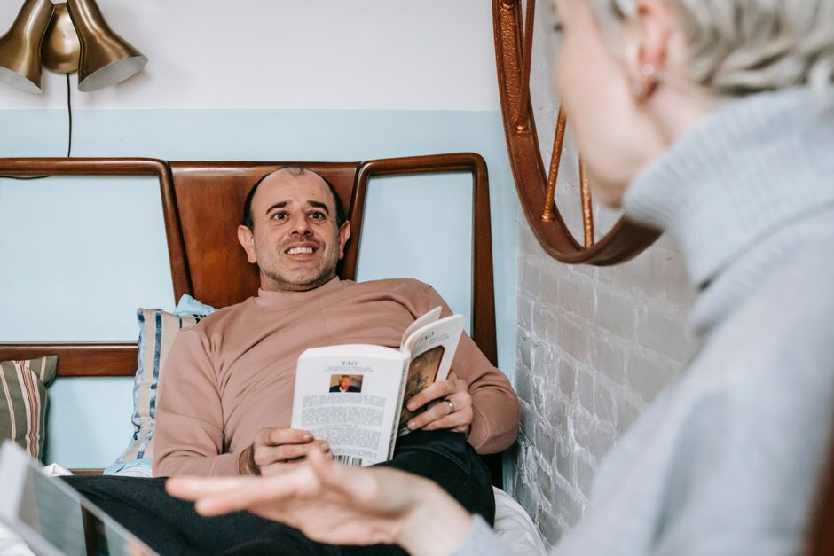 A husband avoids eye contact and buries himself in a book while his wife tries to talk to him.