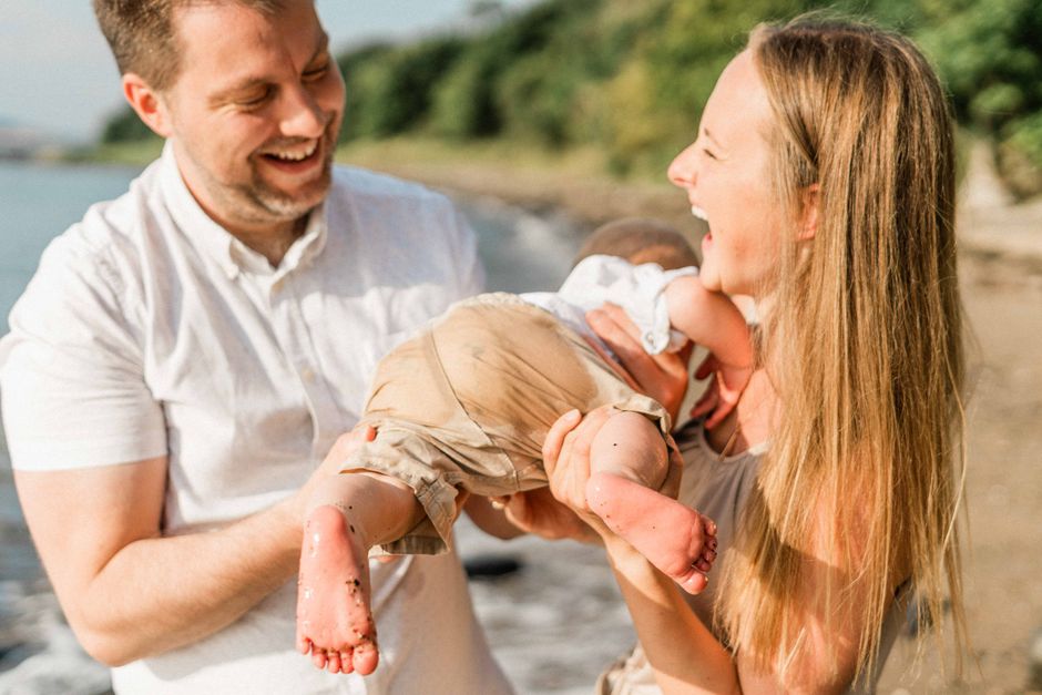 A dad laughs and plays easily with his baby on the beach, a lighthearted bond that can highlight how some husbands connect more freely with their kids than with their spouse.