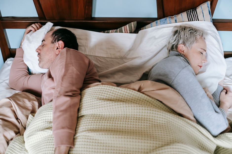 A husband and wife lie turned away from each other in bed, each sleeping on their own schedule.