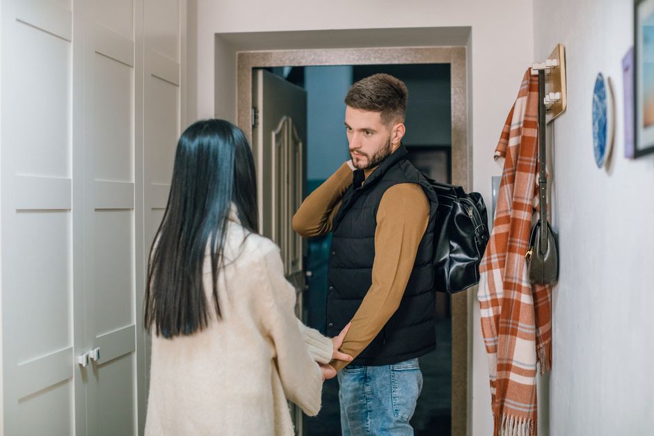 A husband prepares to walk out the door, emotionally distant, while his wife tries to hold on to the moment.