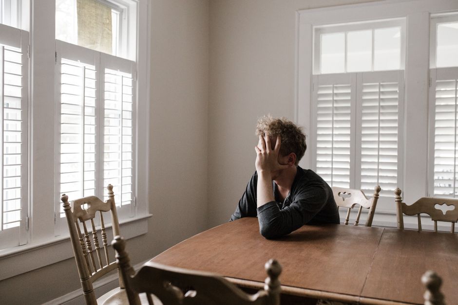 A man sits alone at a table, holding his head in quiet sorrow, hiding a loneliness deeper than he shows.