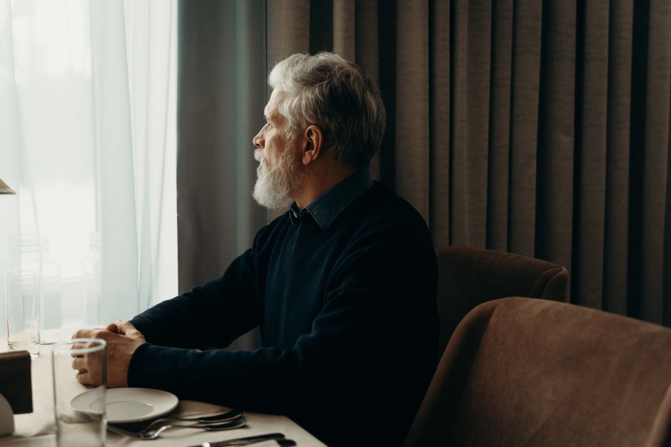 A man sits quietly by a window, lost in thought, perhaps missing someone he doesn't talk about.