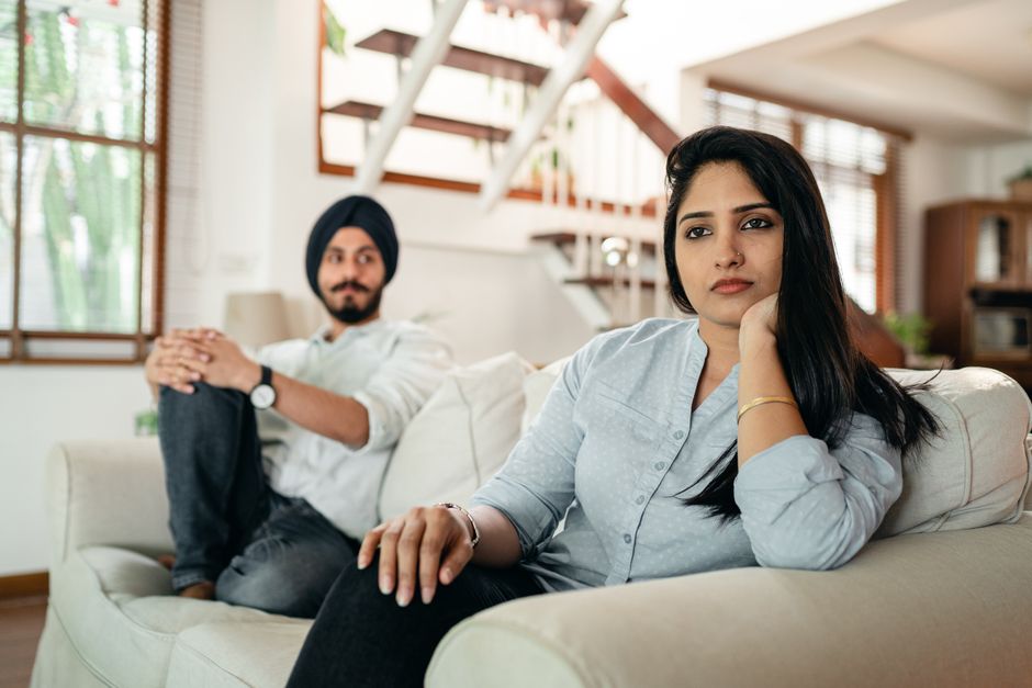 A couple sitting apart on the couch, distant and disconnected, hinting that weekend plans together have become a thing of the past.