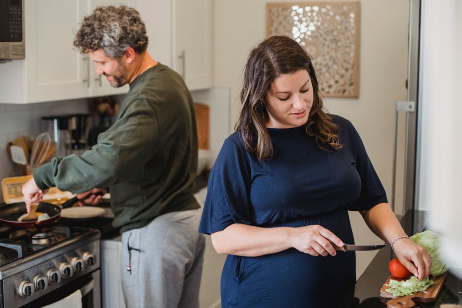 A husband focuses silently on cooking while his wife works quietly beside him, each absorbed in their own task without conversation.