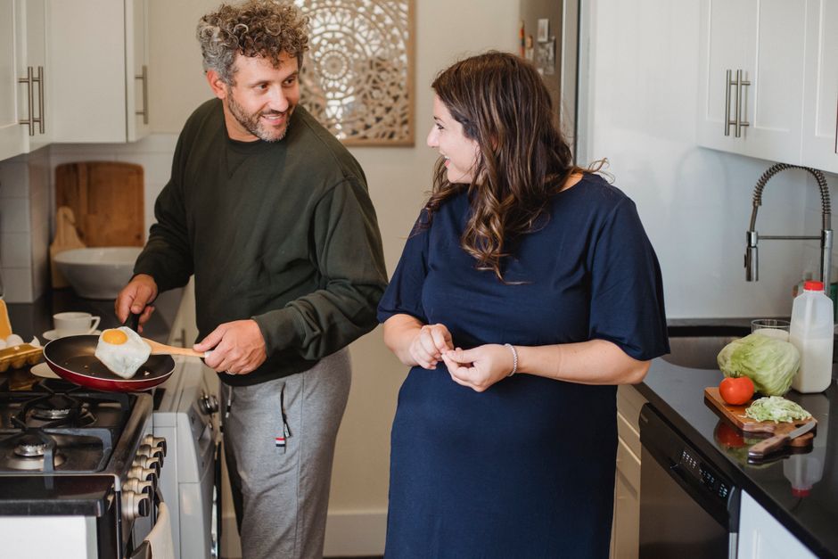 A wife smiles warmly as her husband cooks his favorite breakfast for her in their kitchen.