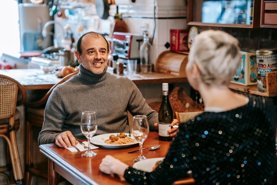 A couple dressed up for a romantic dinner date, smiling and enjoying wine together at a cozy restaurant table.