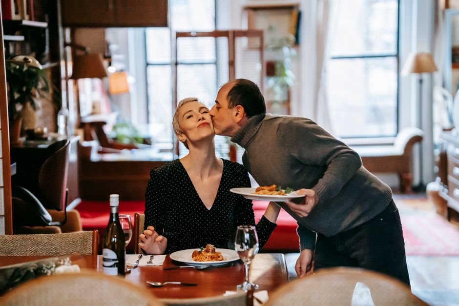 A husband kisses his wife affectionately during a phone-free dinner at home.