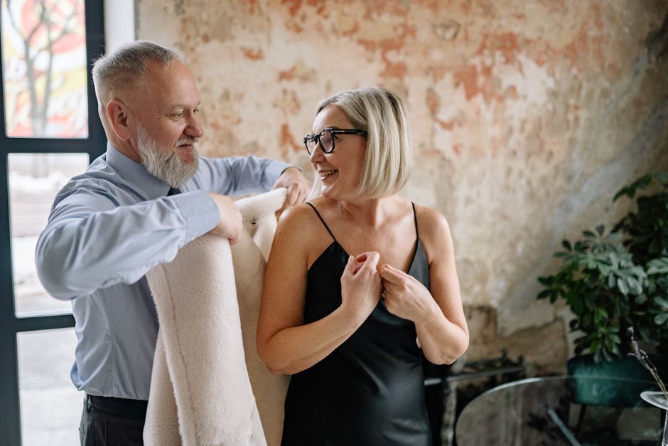 A husband helping his wife get dressed up together on an ordinary day at home.