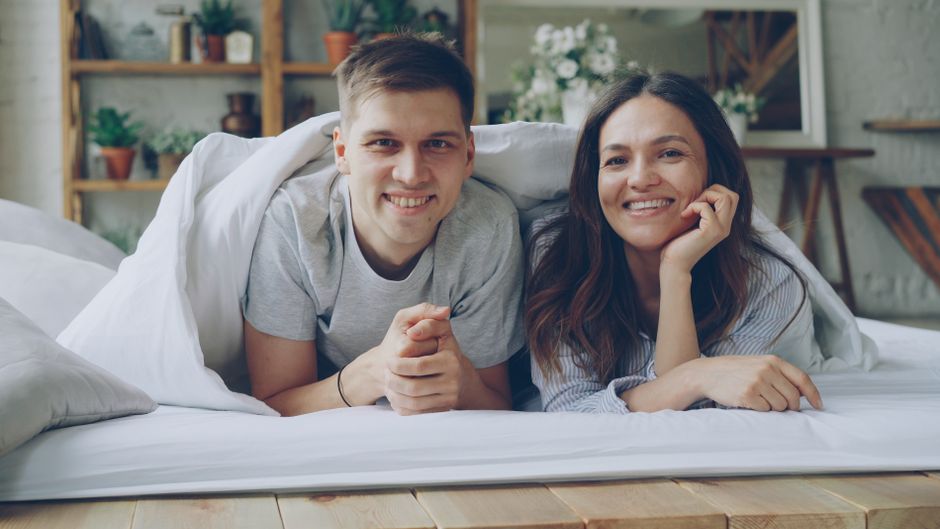 A happy couple greets each other with a smile in bed first thing in the morning.