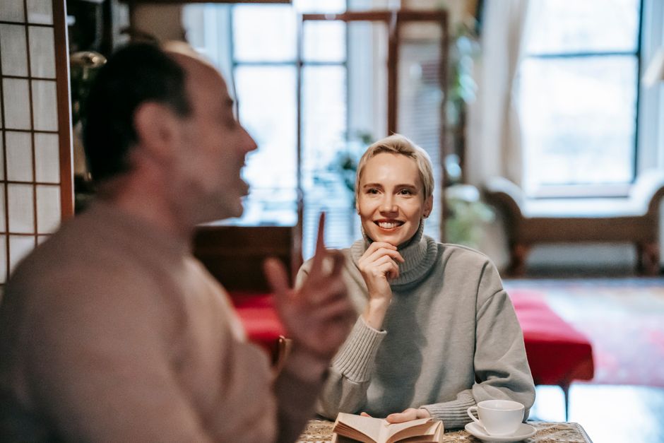 A husband and wife share an attentive conversation over coffee, with her listening closely as he speaks, letting him finish his thought.