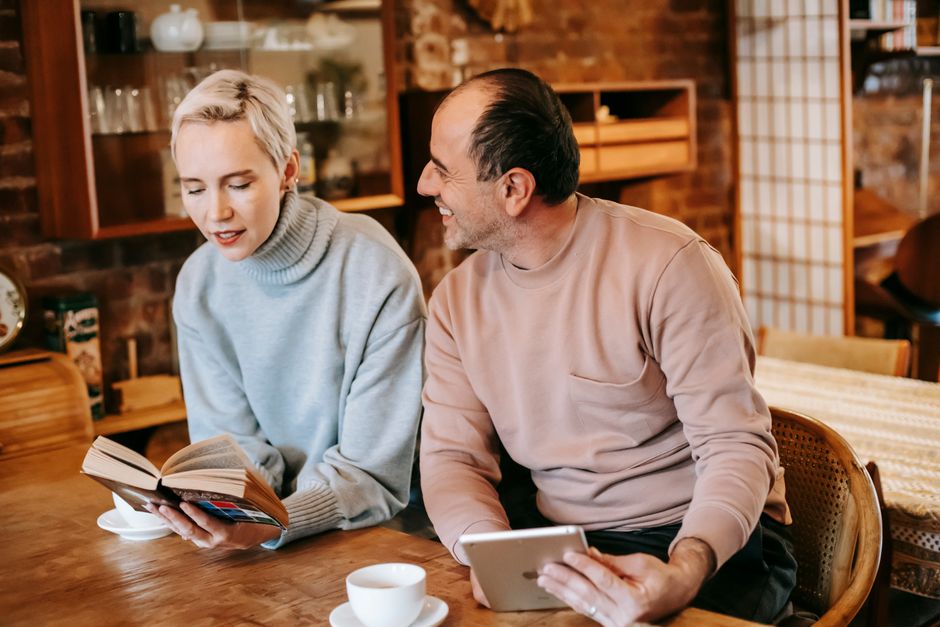A wife shares a quiet moment reading while her husband happily engages with her over his tablet.