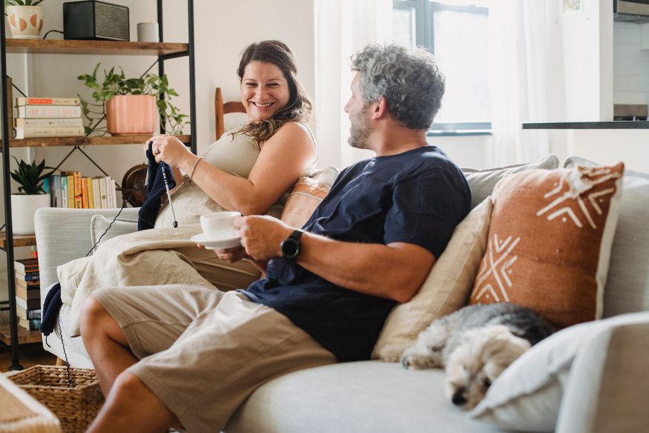 A happy couple laughs together on the couch, enjoying each other's company instead of sweating the small stuff.