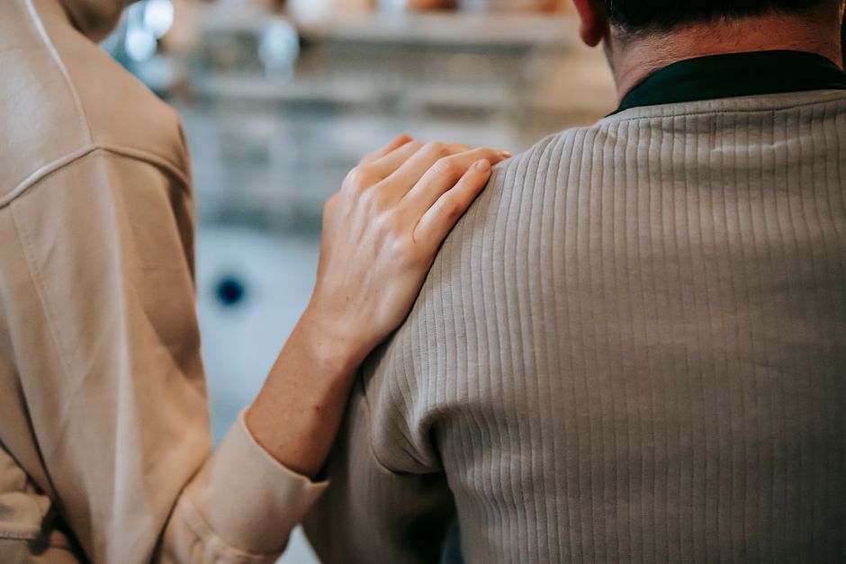 A woman tenderly touches her husband's shoulder as a small gesture of love.