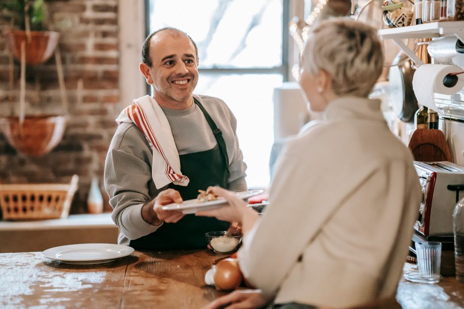 A husband happily serves his wife a home-cooked meal in the kitchen.