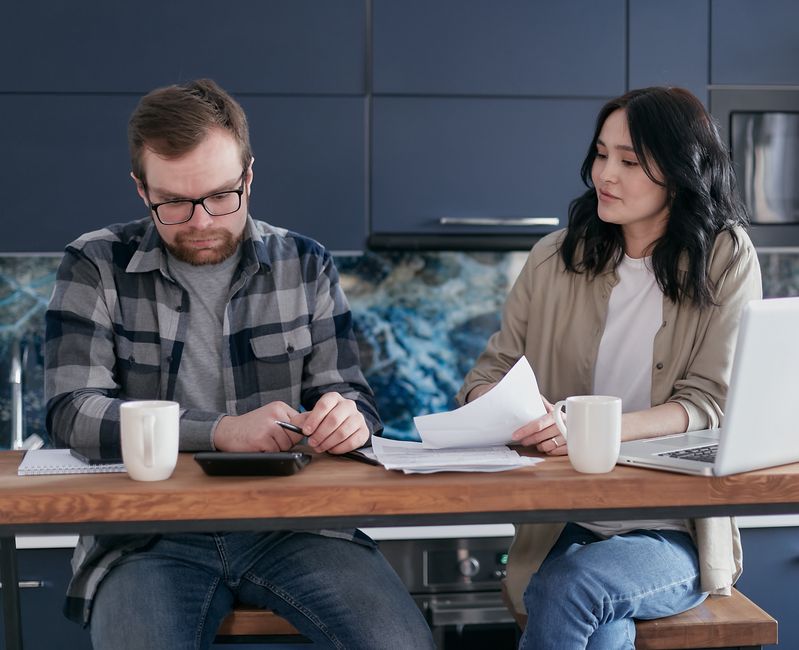 A man quietly crunches numbers over household bills, hinting at the financial worries he keeps to himself.