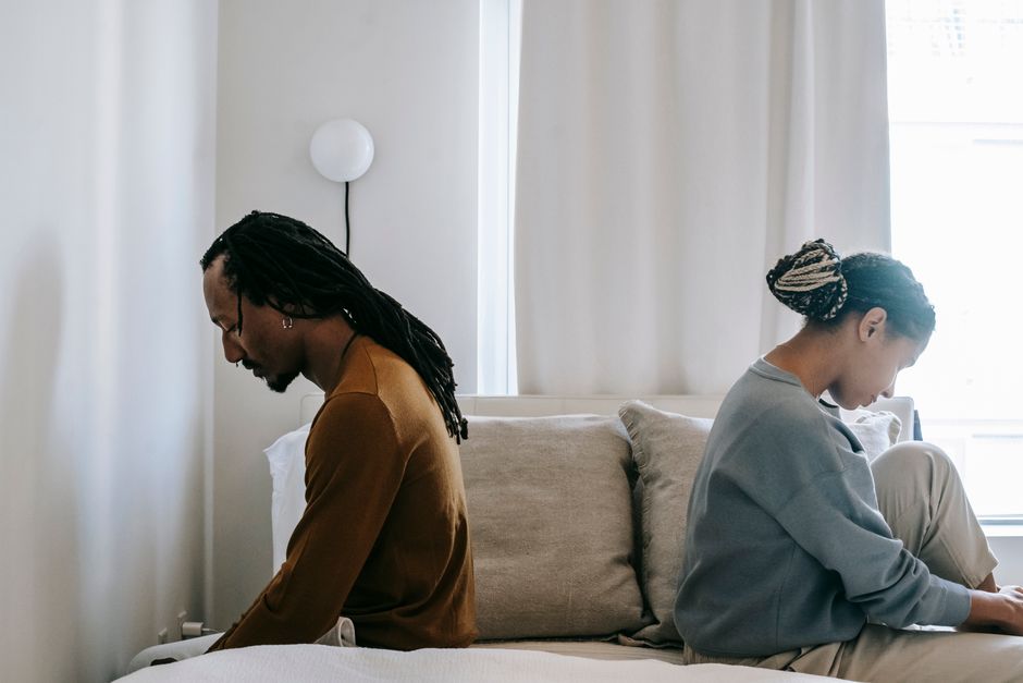 A couple sits back-to-back in silence, avoiding the hard conversation they keep putting off until later.